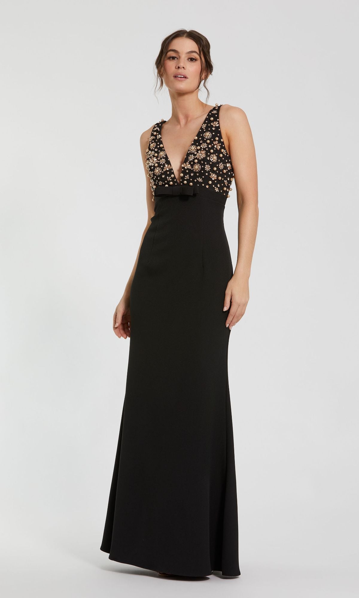 A woman wears the Beaded-Bodice Long Prom Dress (Mac Duggal 2278), an elegant sleeveless black gown featuring a floor-length skirt, deep V-neck, and a beaded bodice with floral embroidery.